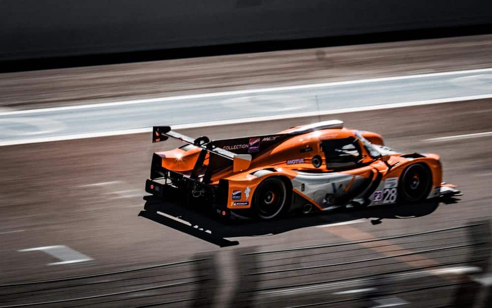 Coche de color naranja en el circuito de Paul Ricard con un fondo de pista y banderas.