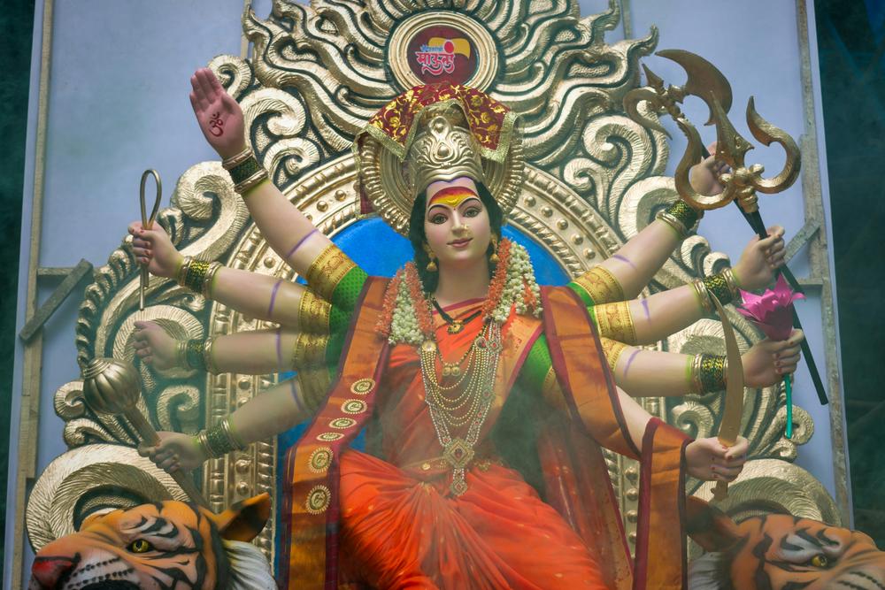 Mujer con un vestido rojo y dorado, representando la divinidad de Maa Durga, en un ambiente festivo y vibrante.