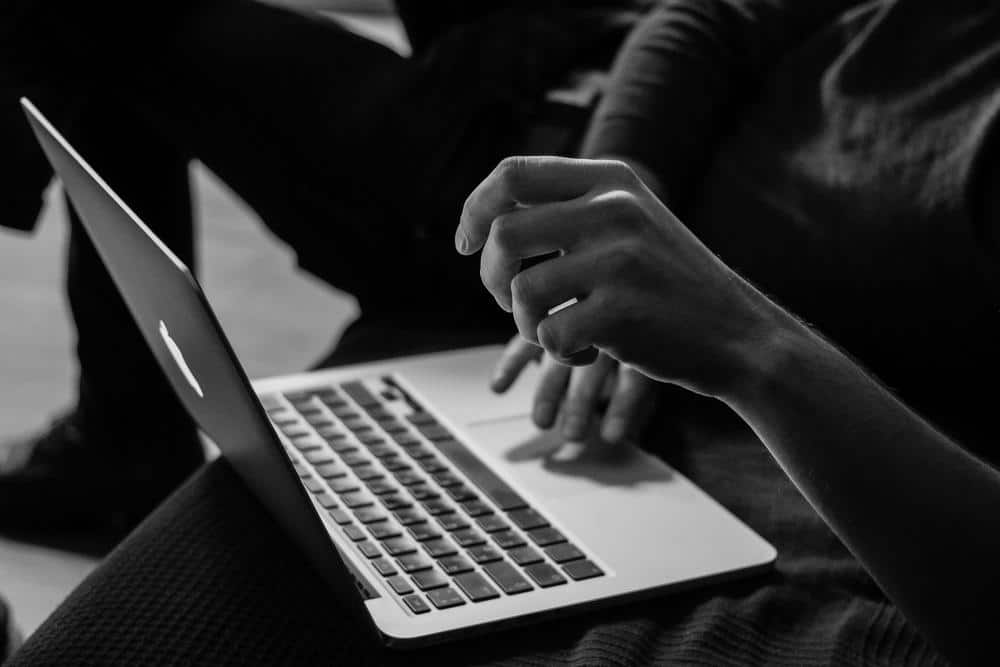 Persona sentada frente a una computadora portátil MacBook en un ambiente iluminado. Notas alineadas en la mesa alrededor. Estilo moderno y minimalista en la decoración. Taza de café al